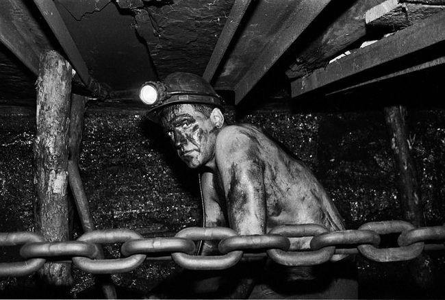 Miner Black and white photo of a shirtless miner in a coal mine, black with coal wearing lighted helmut, chain in foreground.